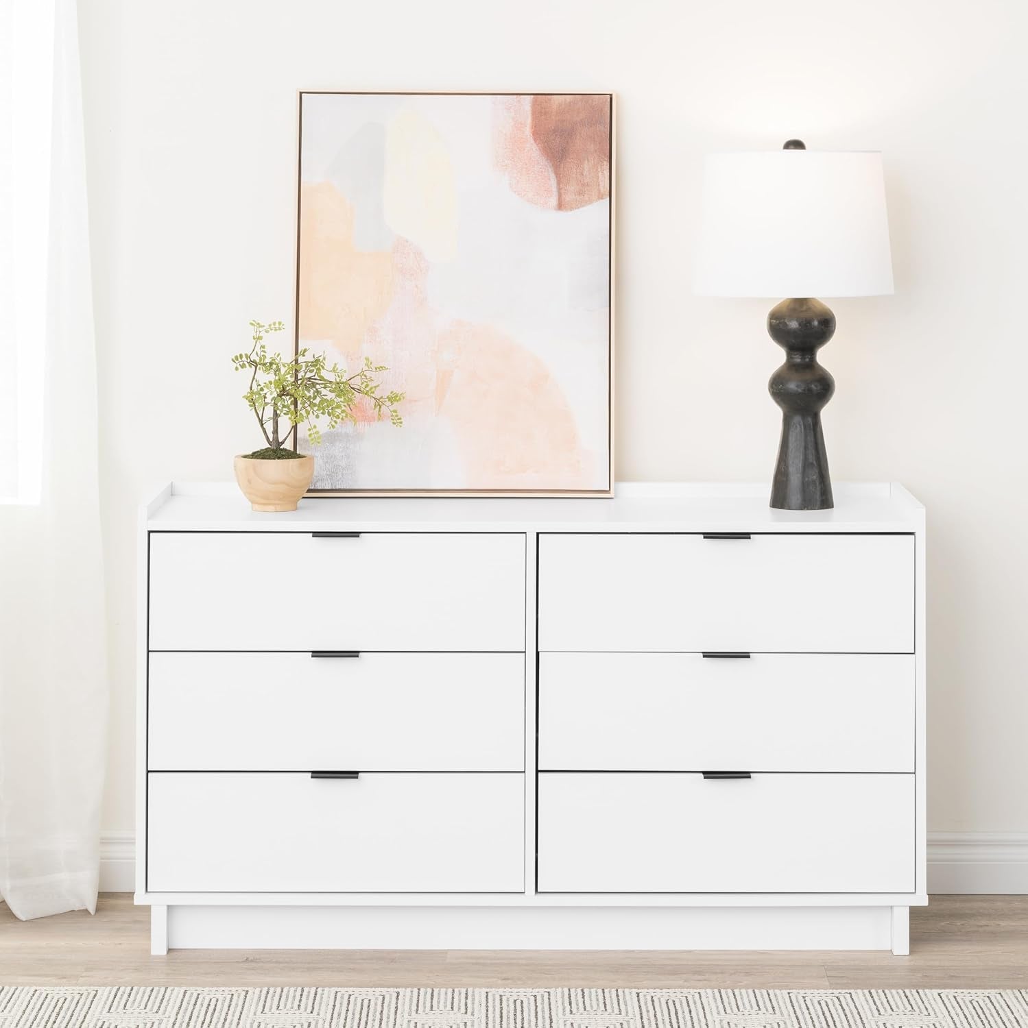 White dresser with a lamp and abstract art in a room.