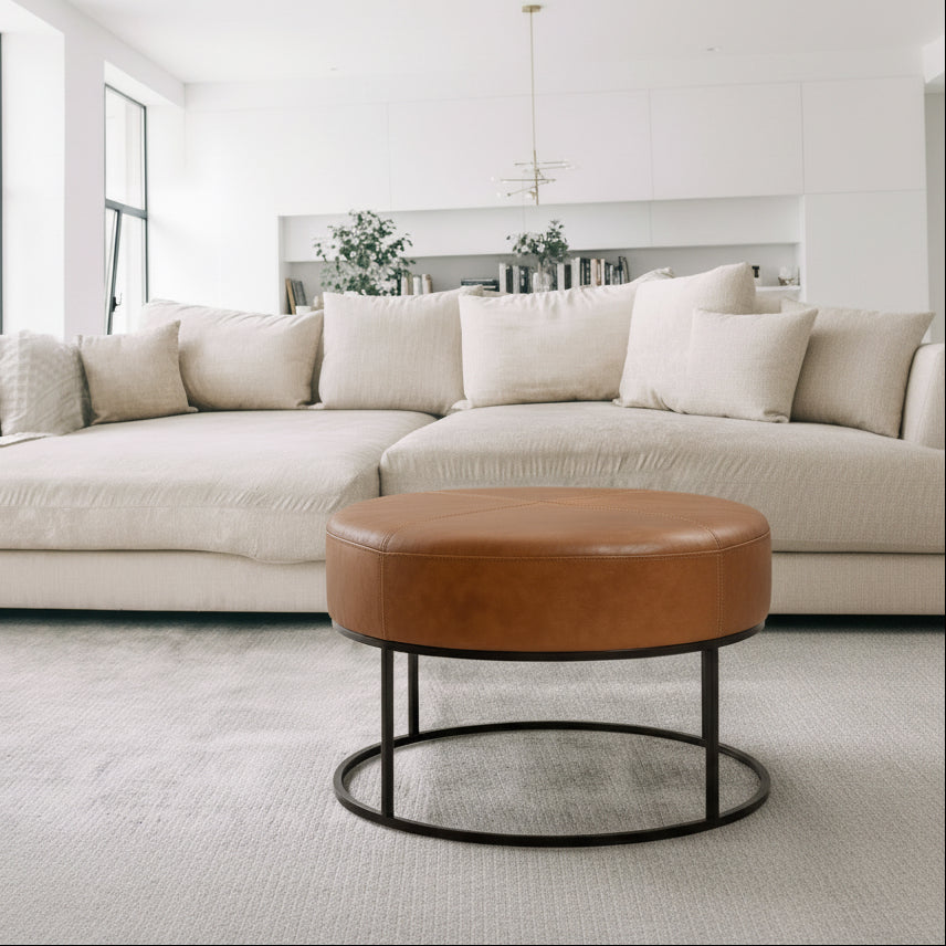 Woman sitting on a brown leather ottoman in a living room.
