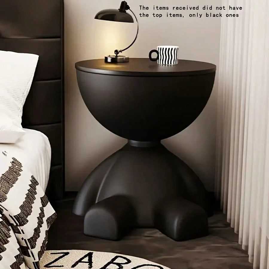 Black side table with a lamp and mug next to a bed in a bedroom setting.