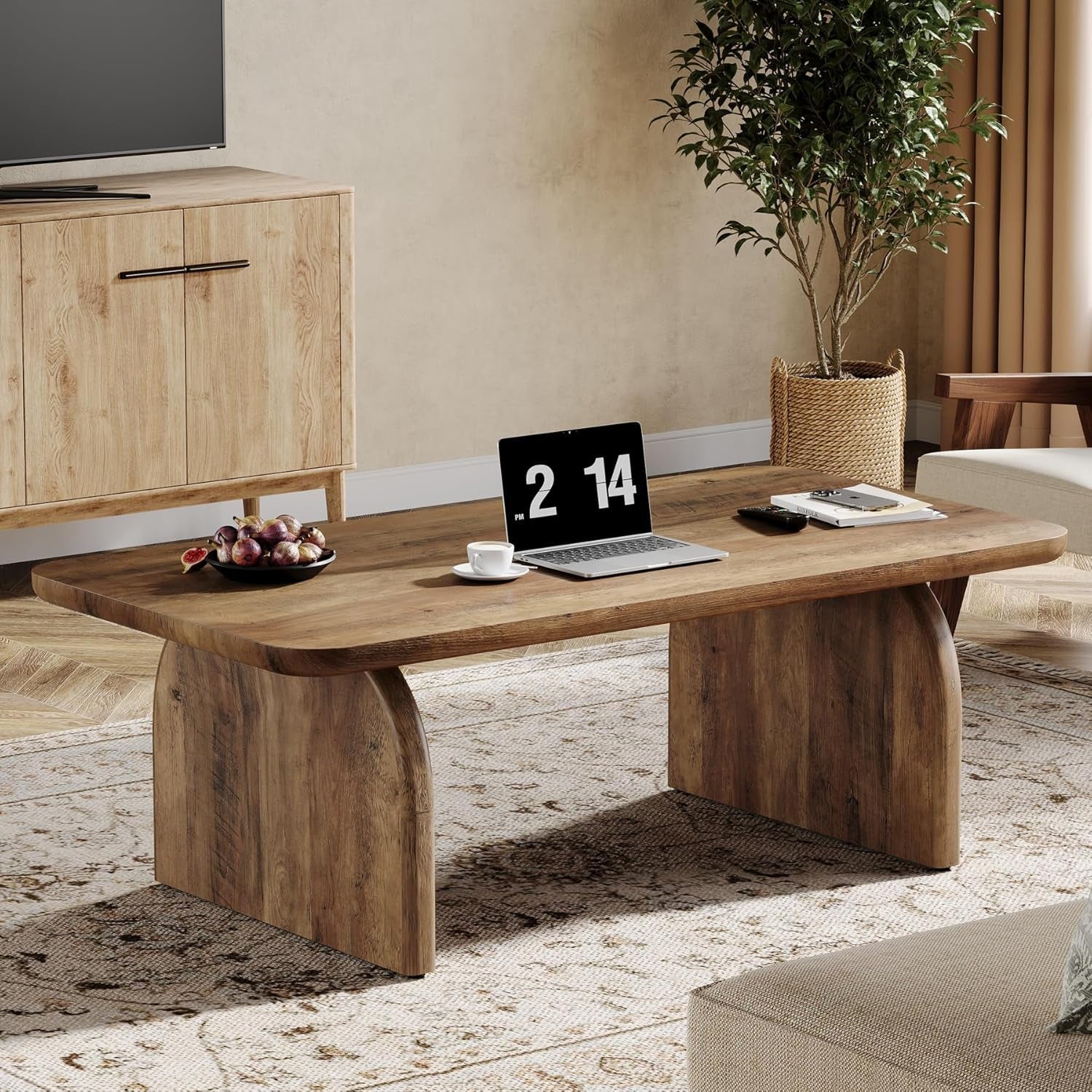 Wooden desk in a living room with a laptop, coffee cup, and fruit bowl.