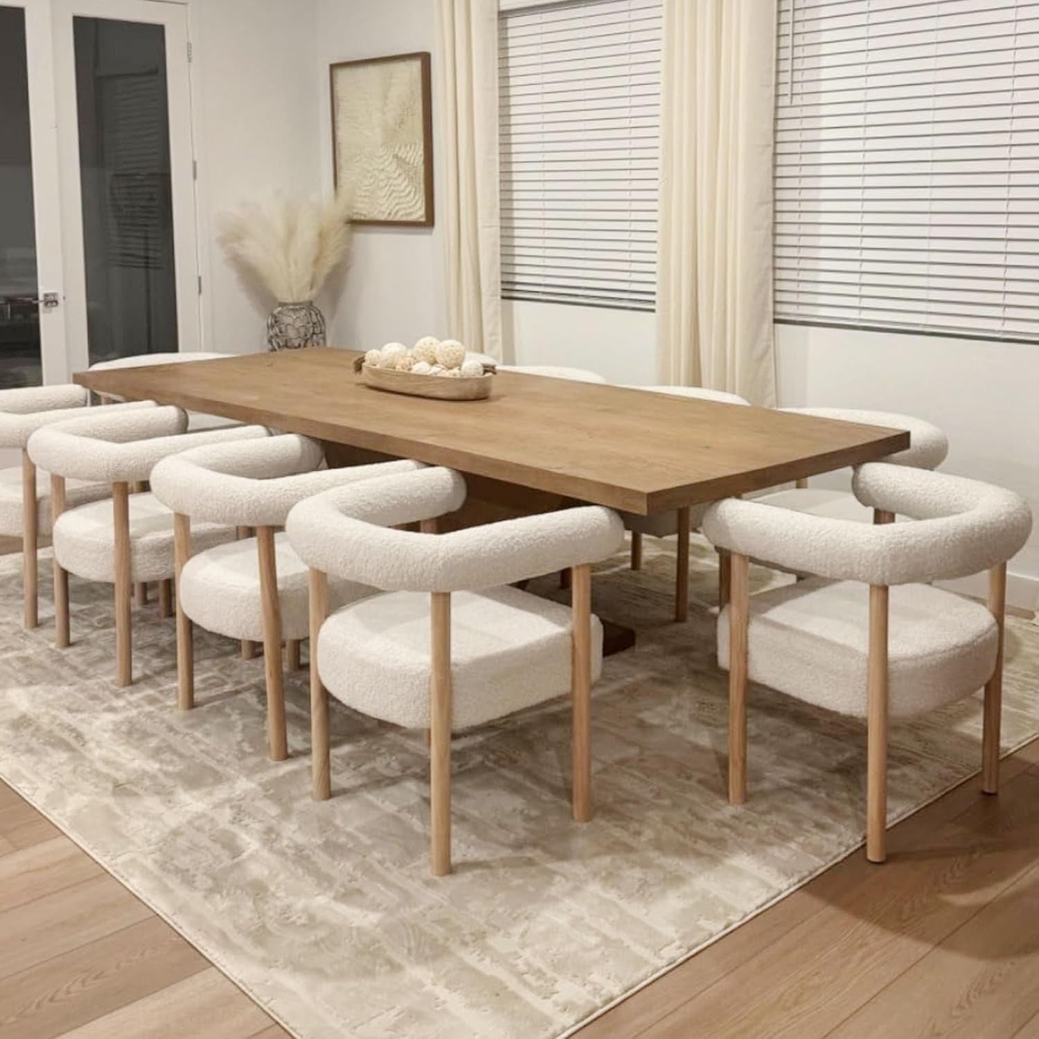 Dining room with wooden table and white chairs on a patterned rug.