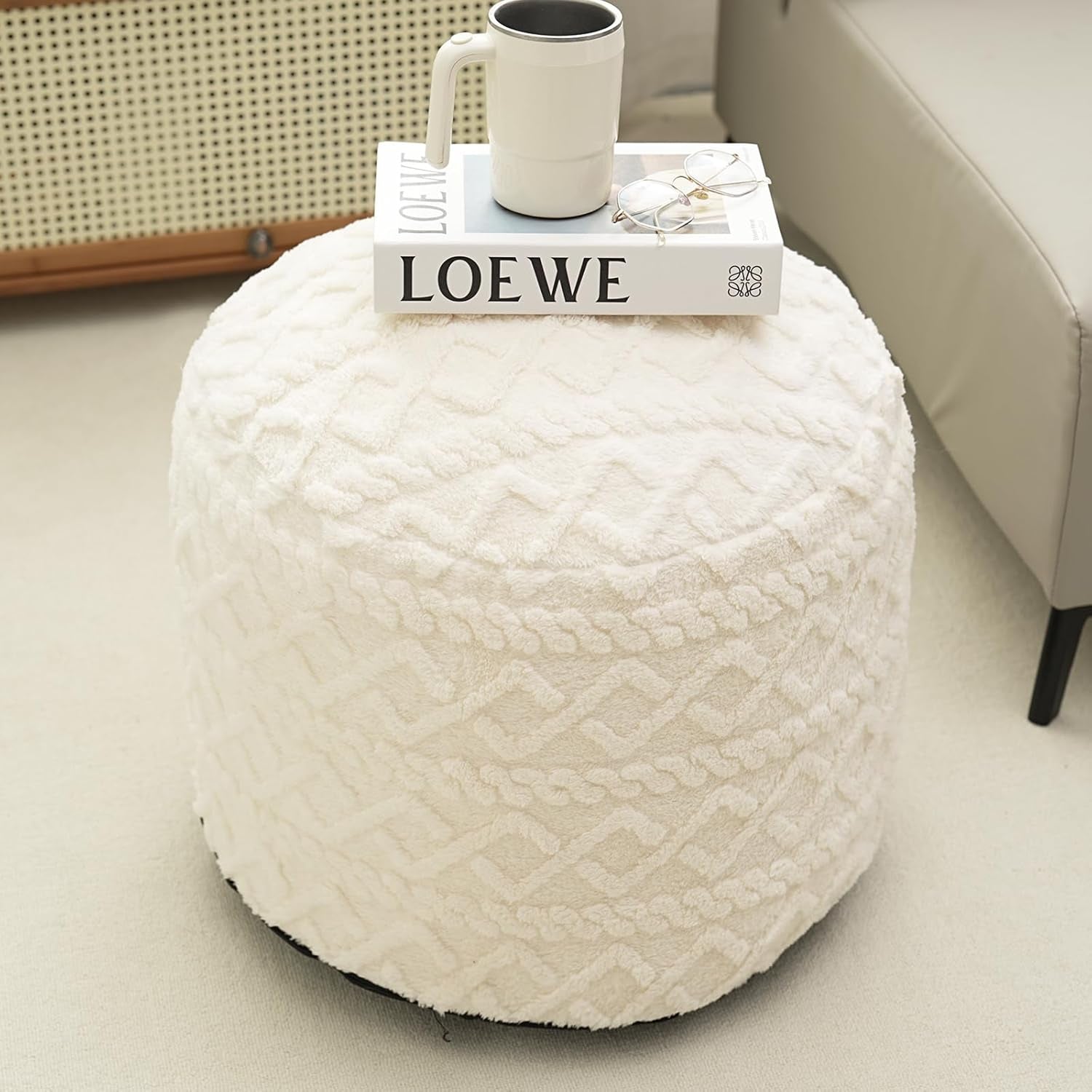 White textured ottoman with a mug and book on top, featuring the LOEWE brand.