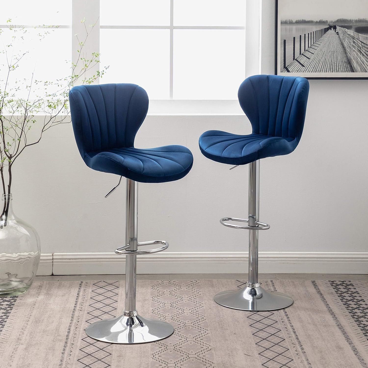 Two blue bar stools with chrome bases in a room with a window and decorative elements.