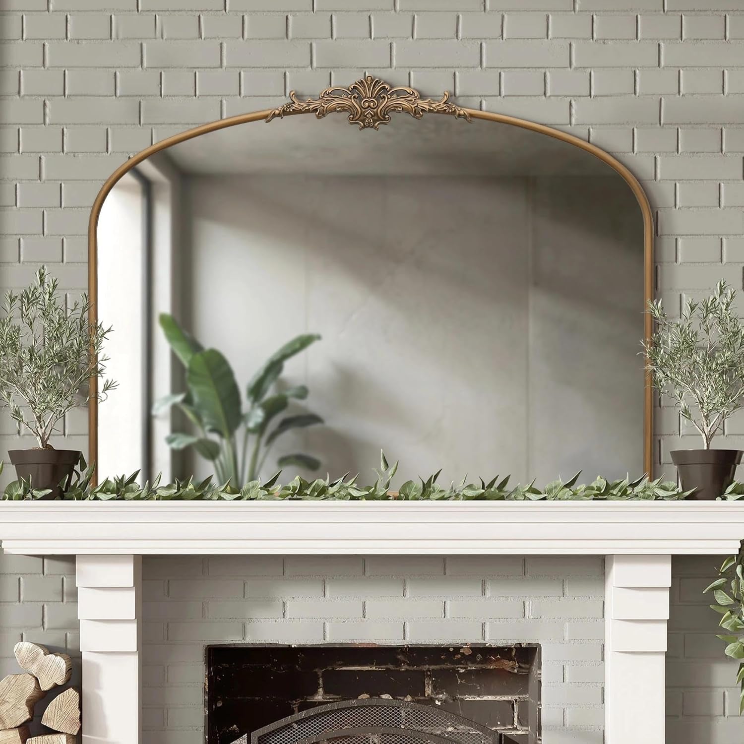 Decorative mirror above a fireplace with plants on a light gray brick wall background