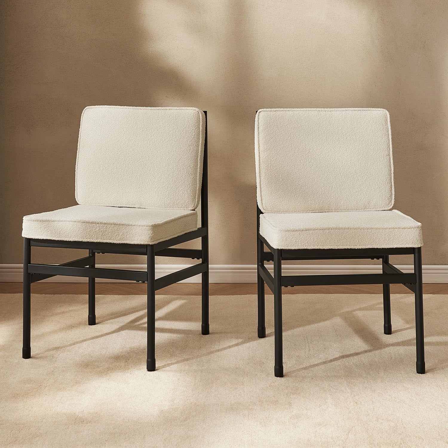 Two beige cushioned chairs with black frames on a beige floor and wall.