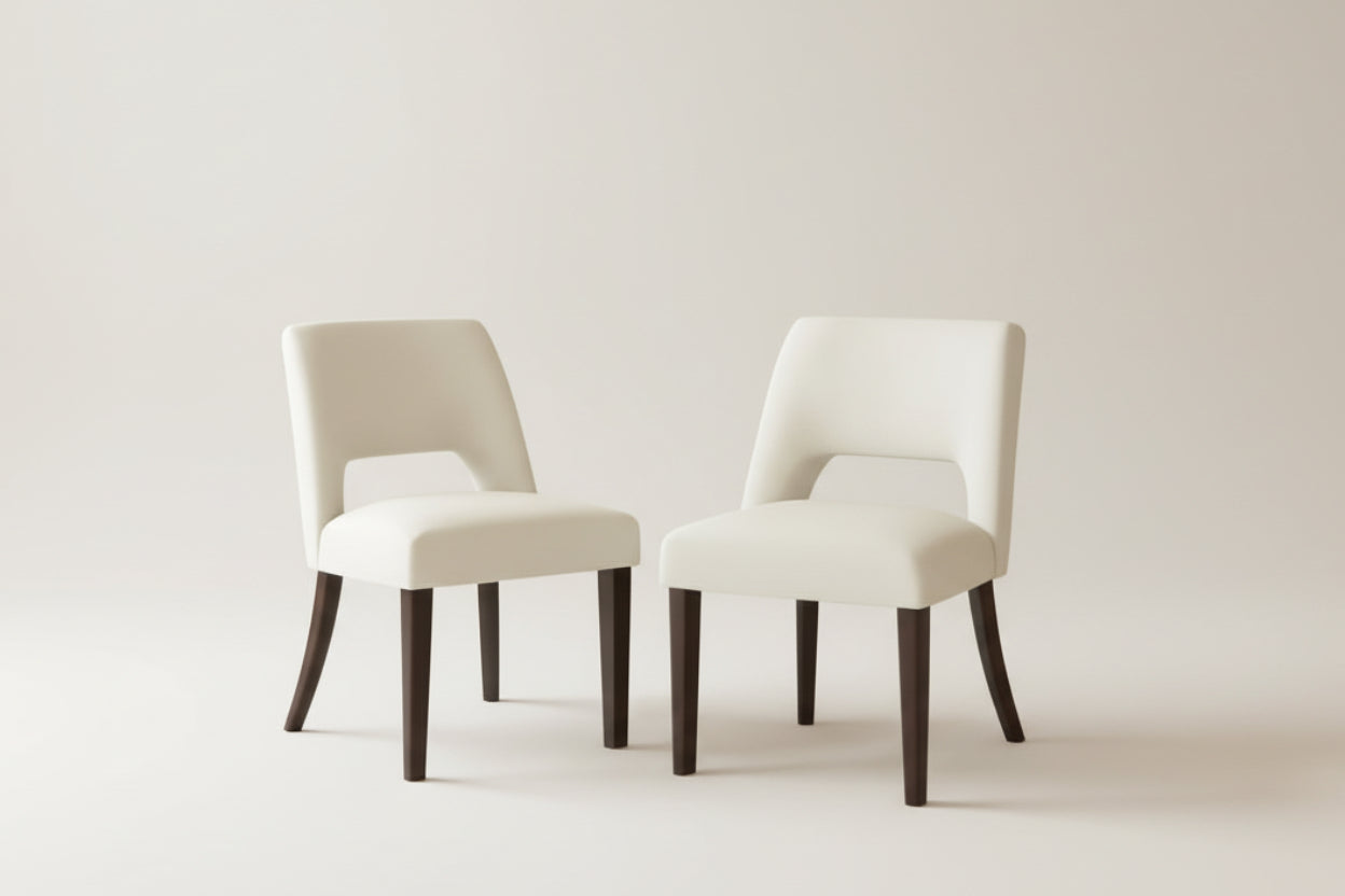 Two white chairs with dark wooden legs on a light rug against an orange wall.