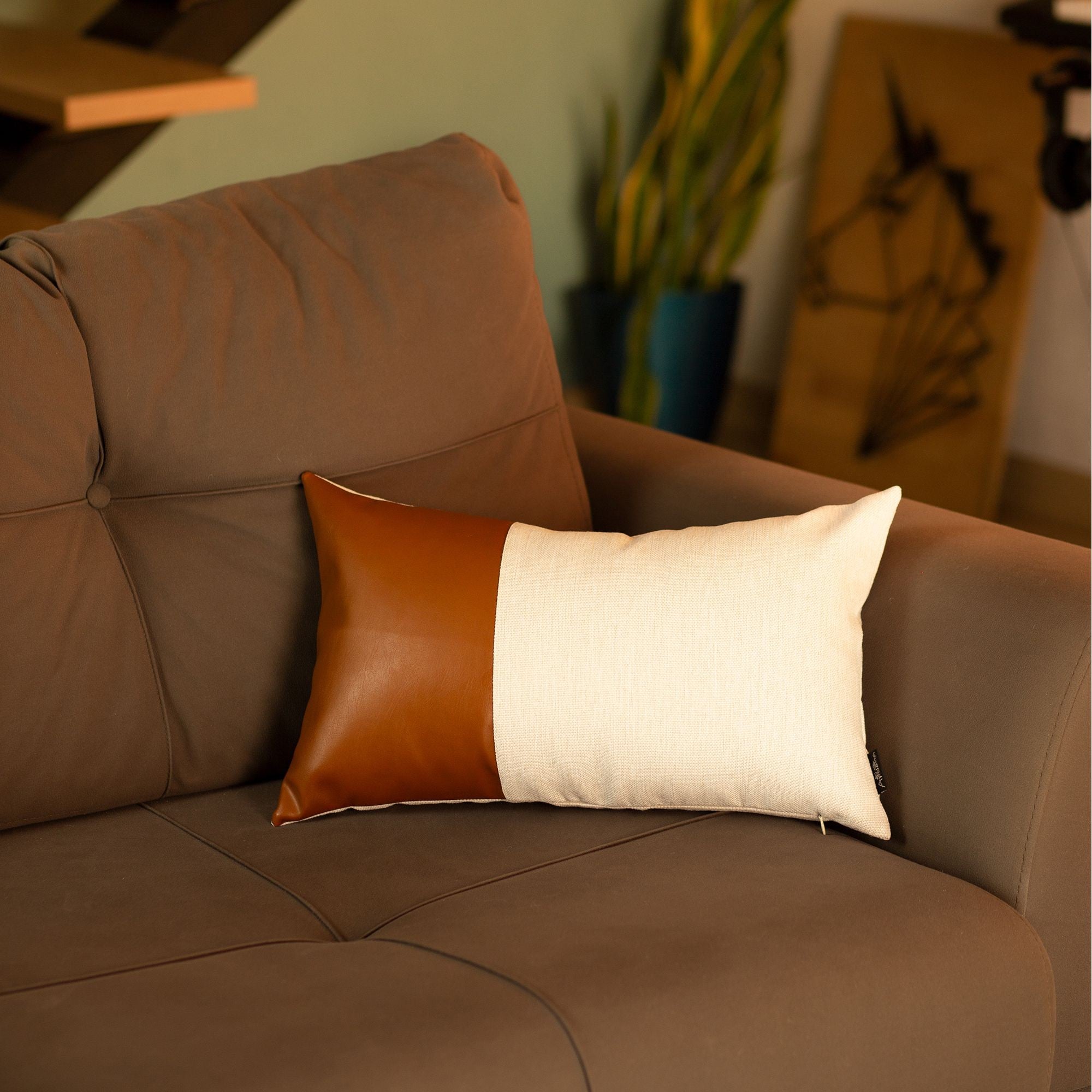 Brown leather sofa with a brown, white, and orange pillow in a living room setting.