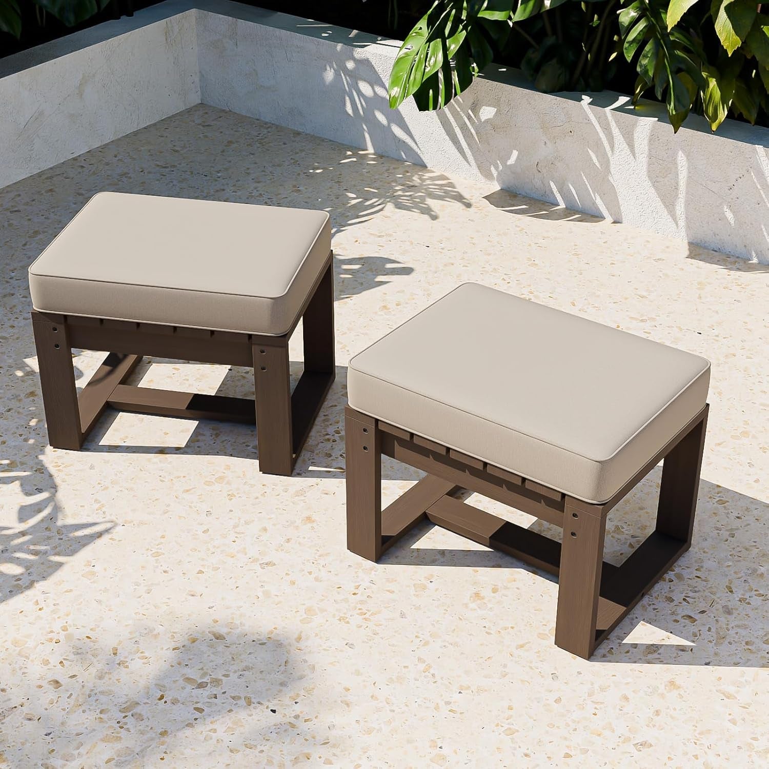 Two outdoor ottomans with beige cushions on a stone patio.