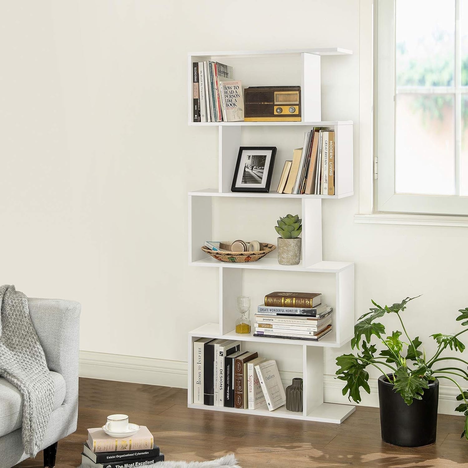 White bookshelf with books and decor items in a room with a window and plant.