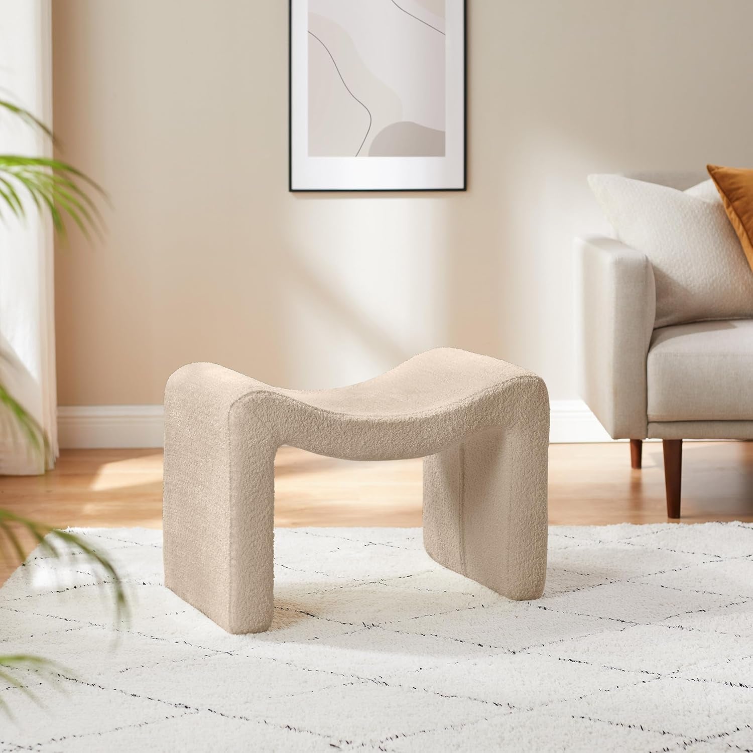 Beige textured stool in a living room setting with a sofa and abstract art on the wall.