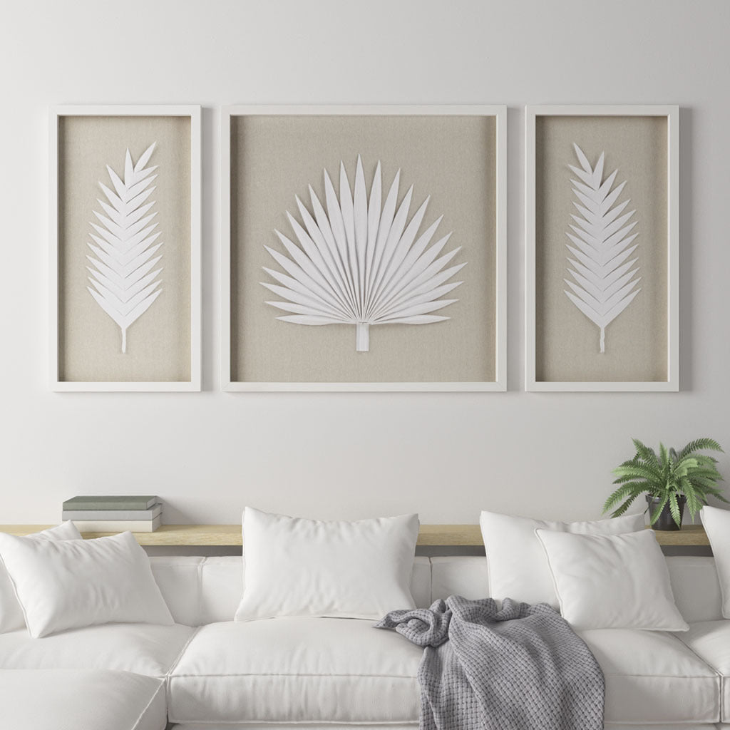 Three framed white leaf prints on a wall above a sofa.