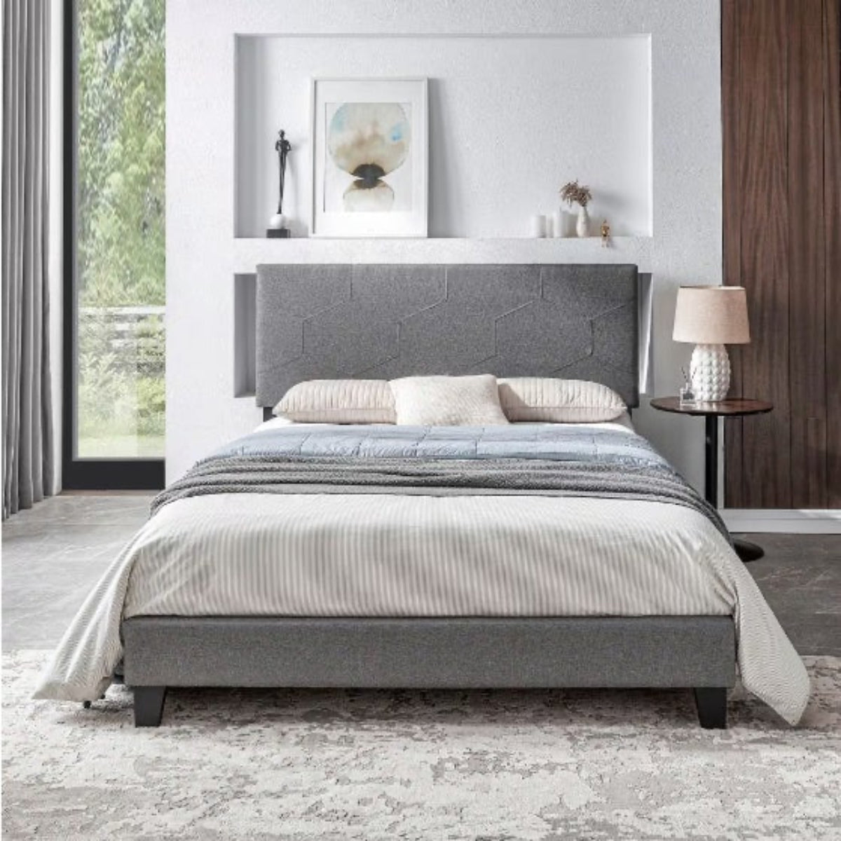Gray upholstered bed in a modern bedroom with a side table and lamp.