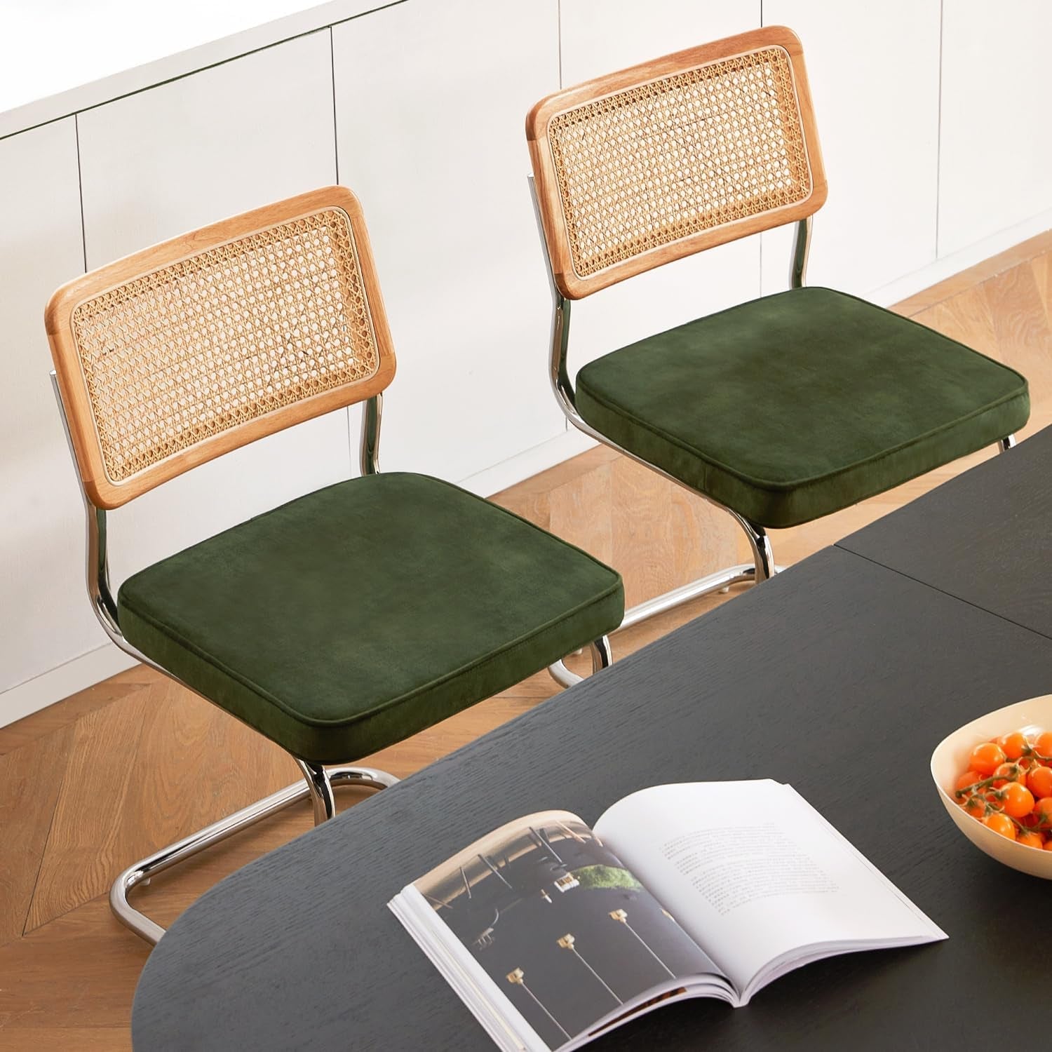 Two green cushioned chairs with wicker backrests in front of a table with an open book and bowl.