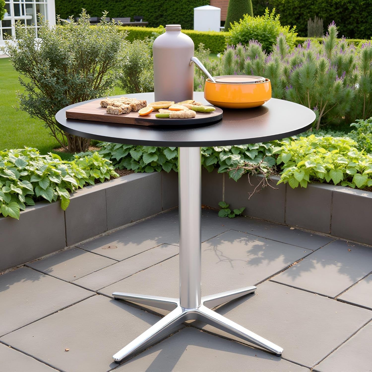 Round outdoor table with a silver base on a patio, surrounded by greenery