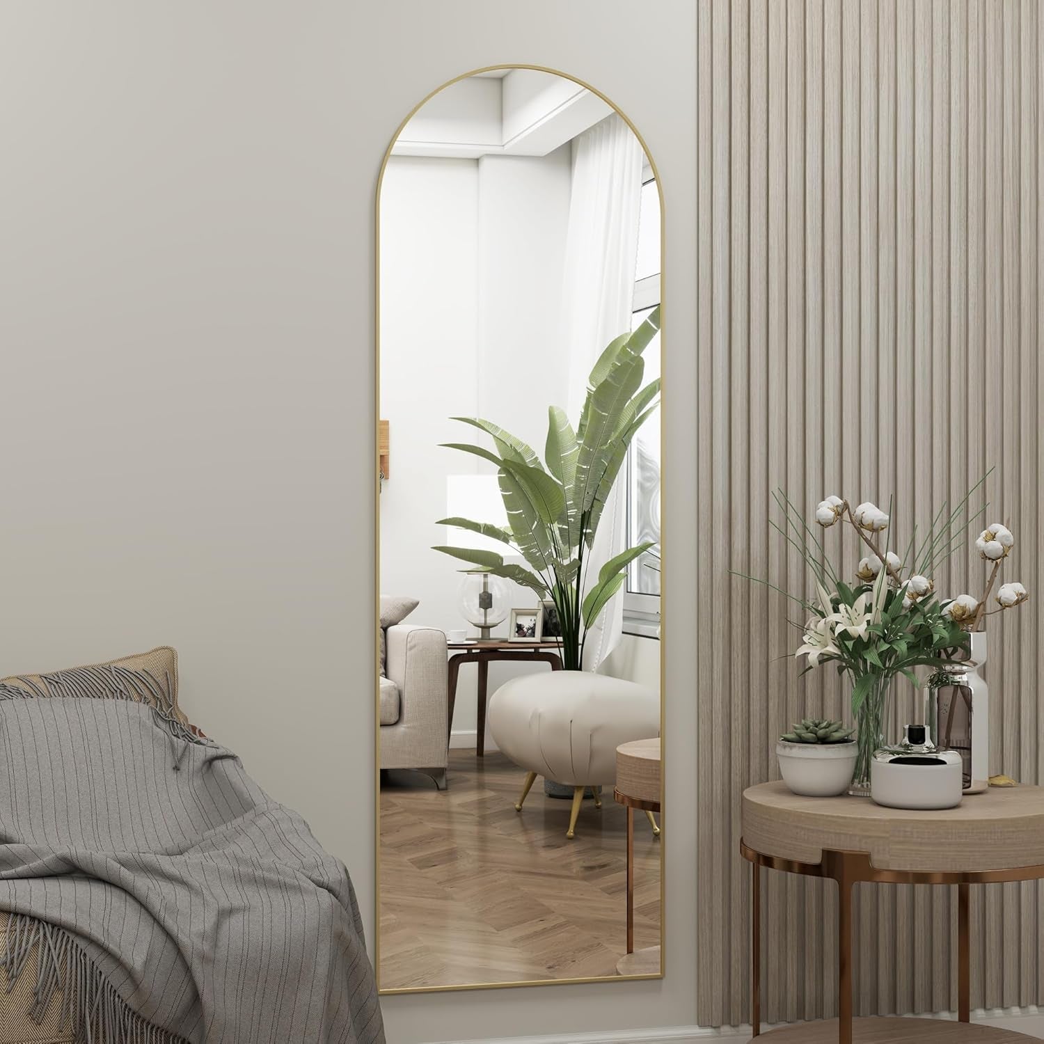 Full-length mirror in a room with a sofa, plant, and small table with flowers.