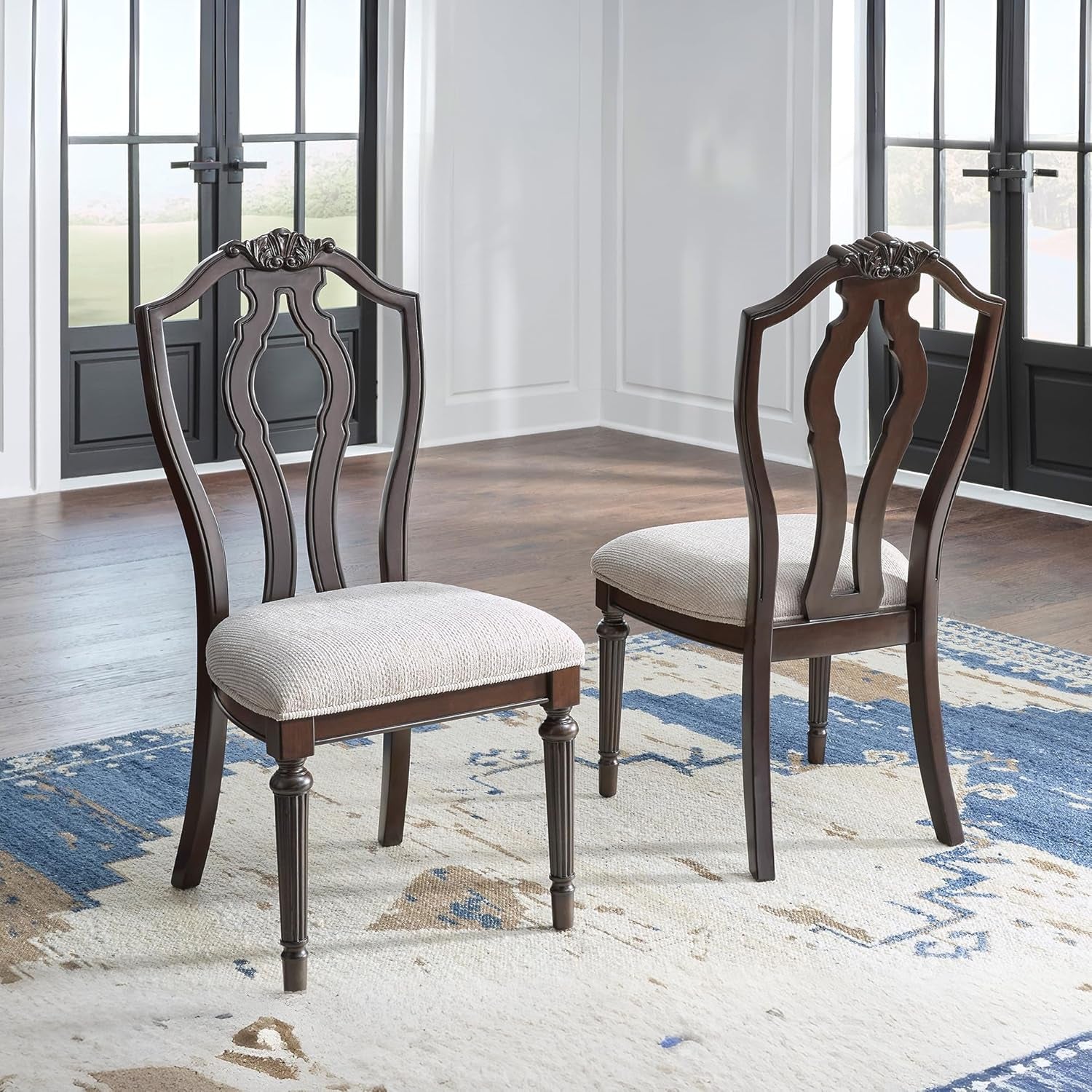 Two wooden chairs with upholstered seats in a room with large windows.