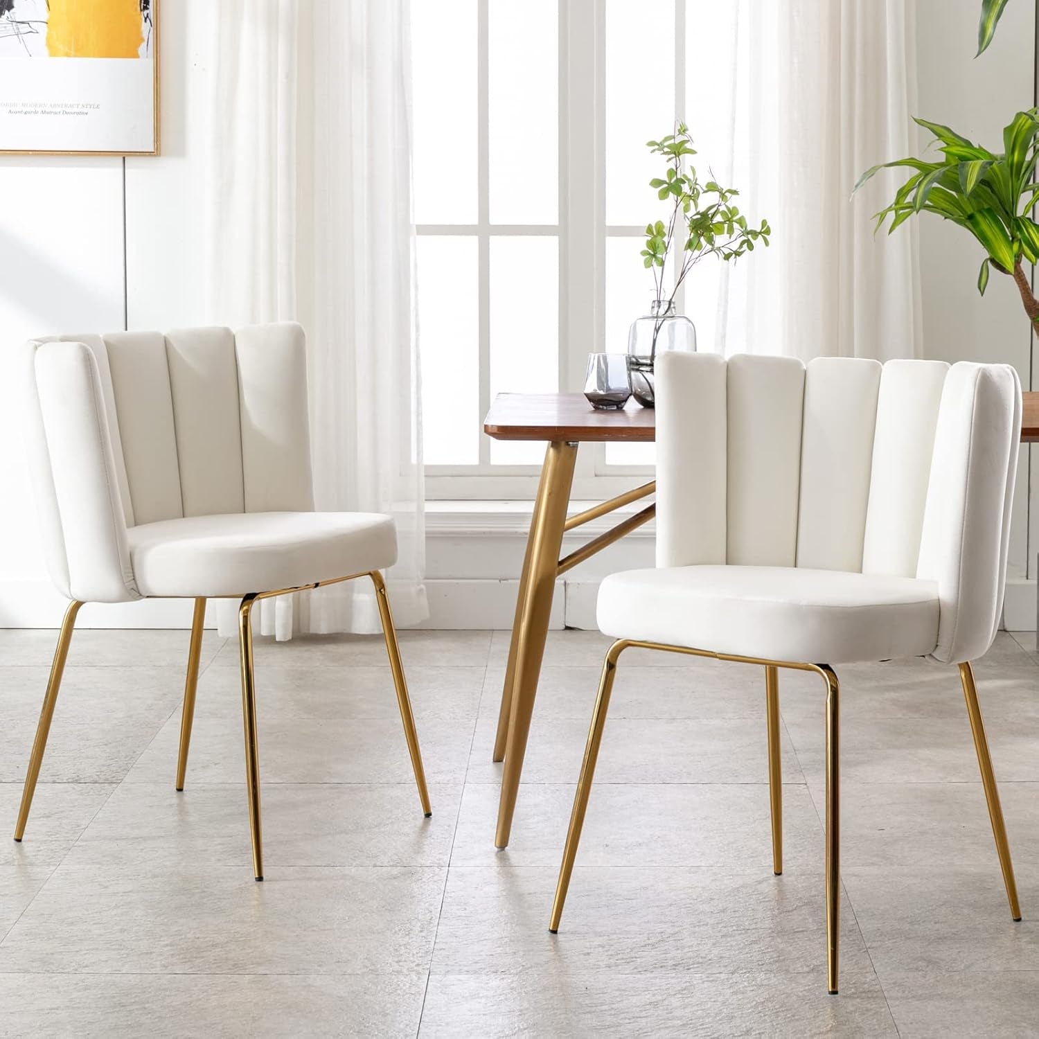 Two white chairs with gold legs in a bright room with a table and plants.