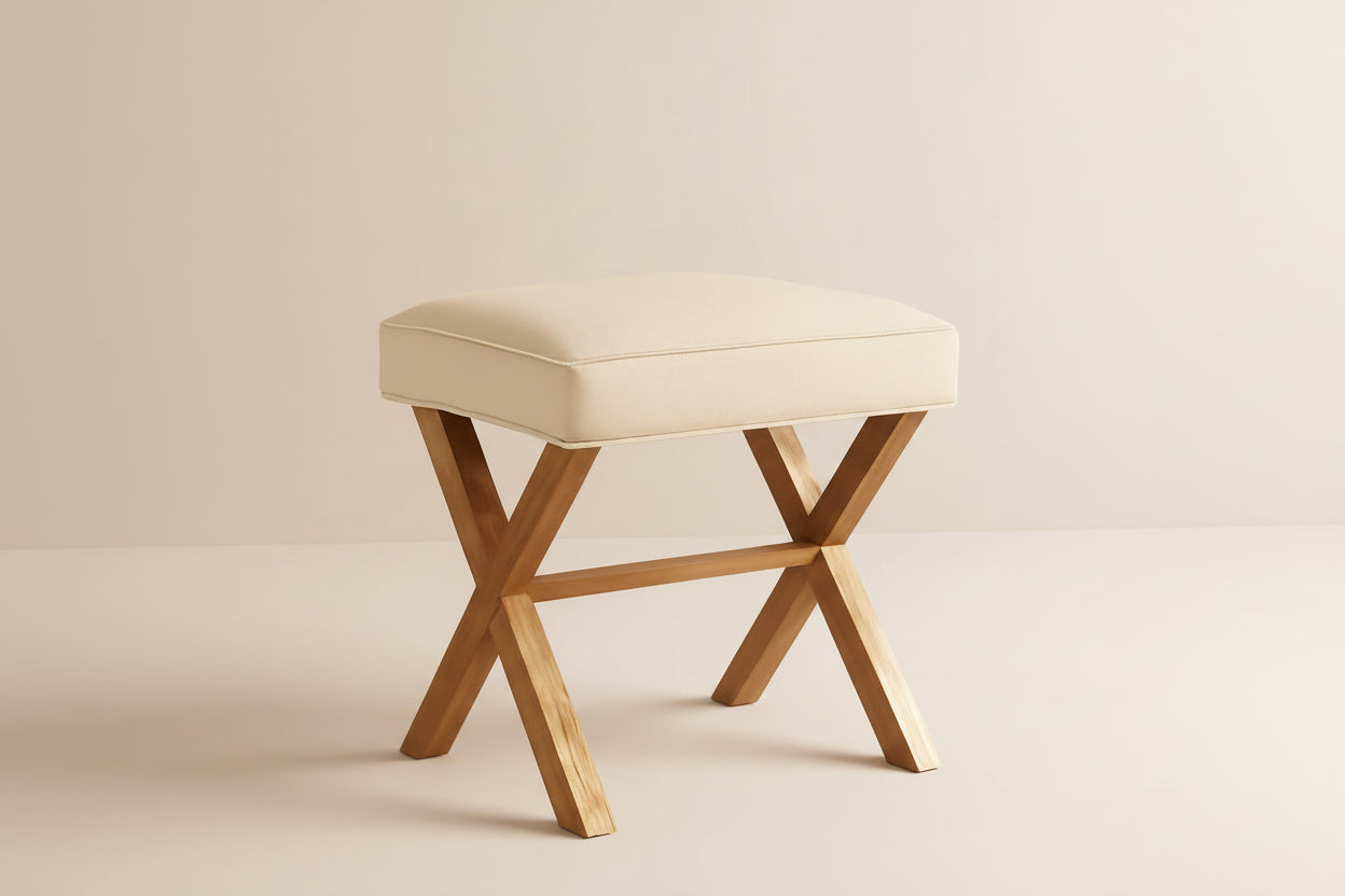 Beige cushioned stool with wooden legs in a room setting.