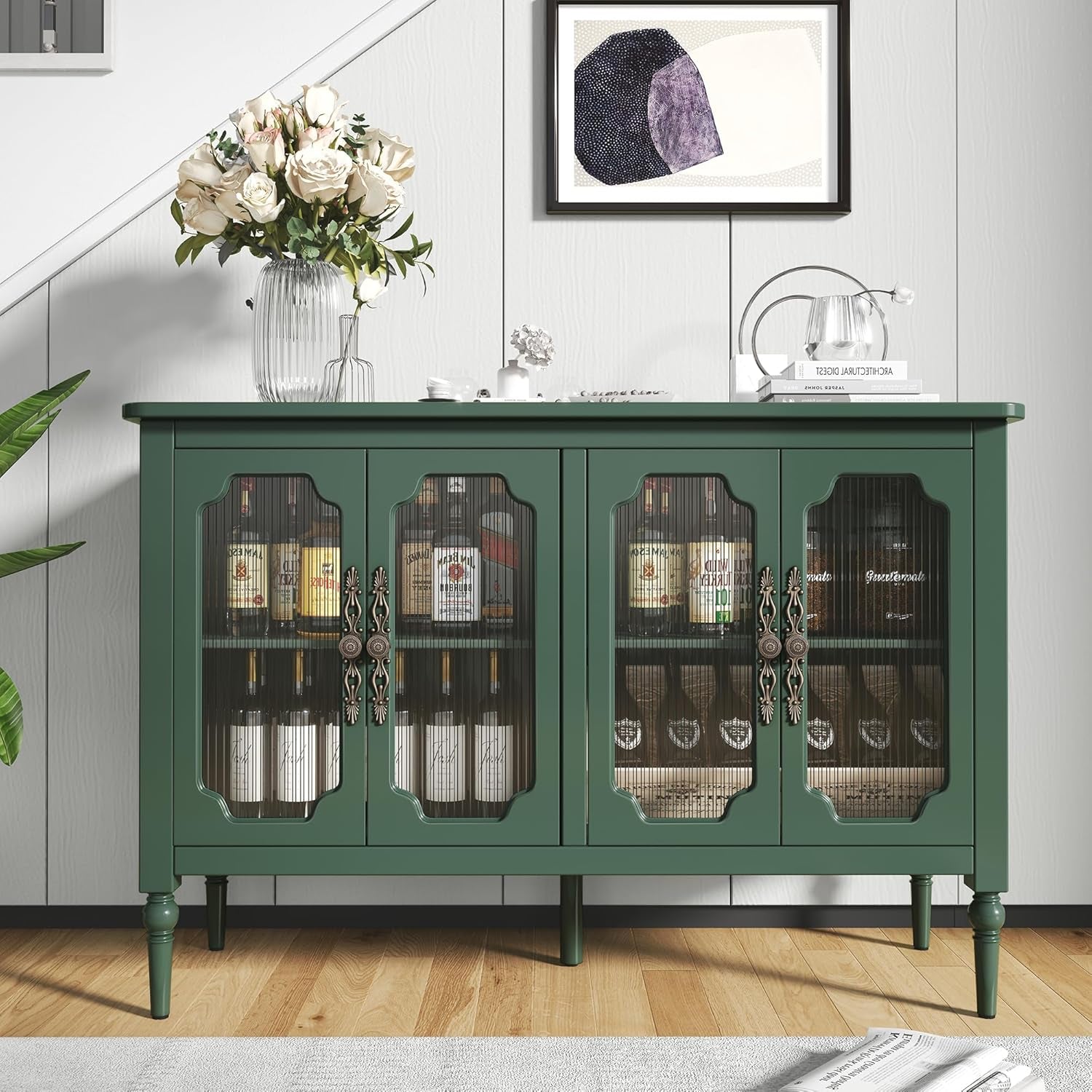 Green sideboard with glass doors displaying bottles in a room with a painting on the wall.