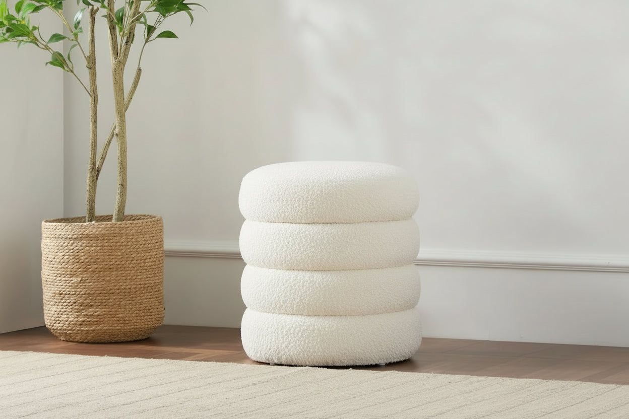 Person sitting on a beige footstool ottoman in a room with a plant and rug.