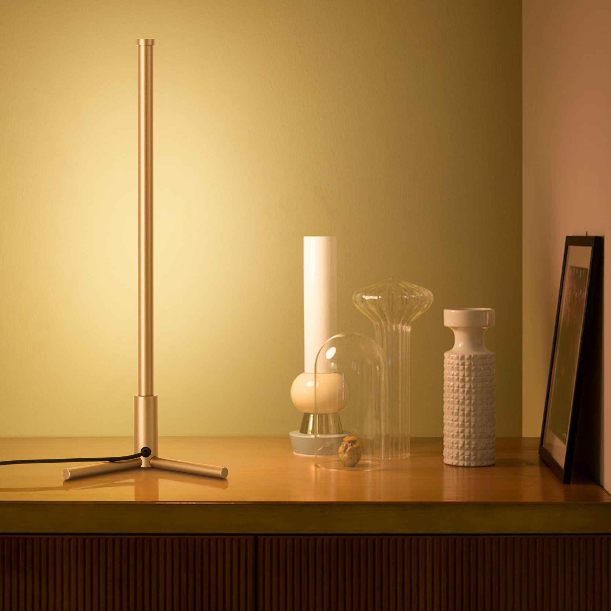 Modern table lamp on a wooden surface with decorative items against a yellow wall.