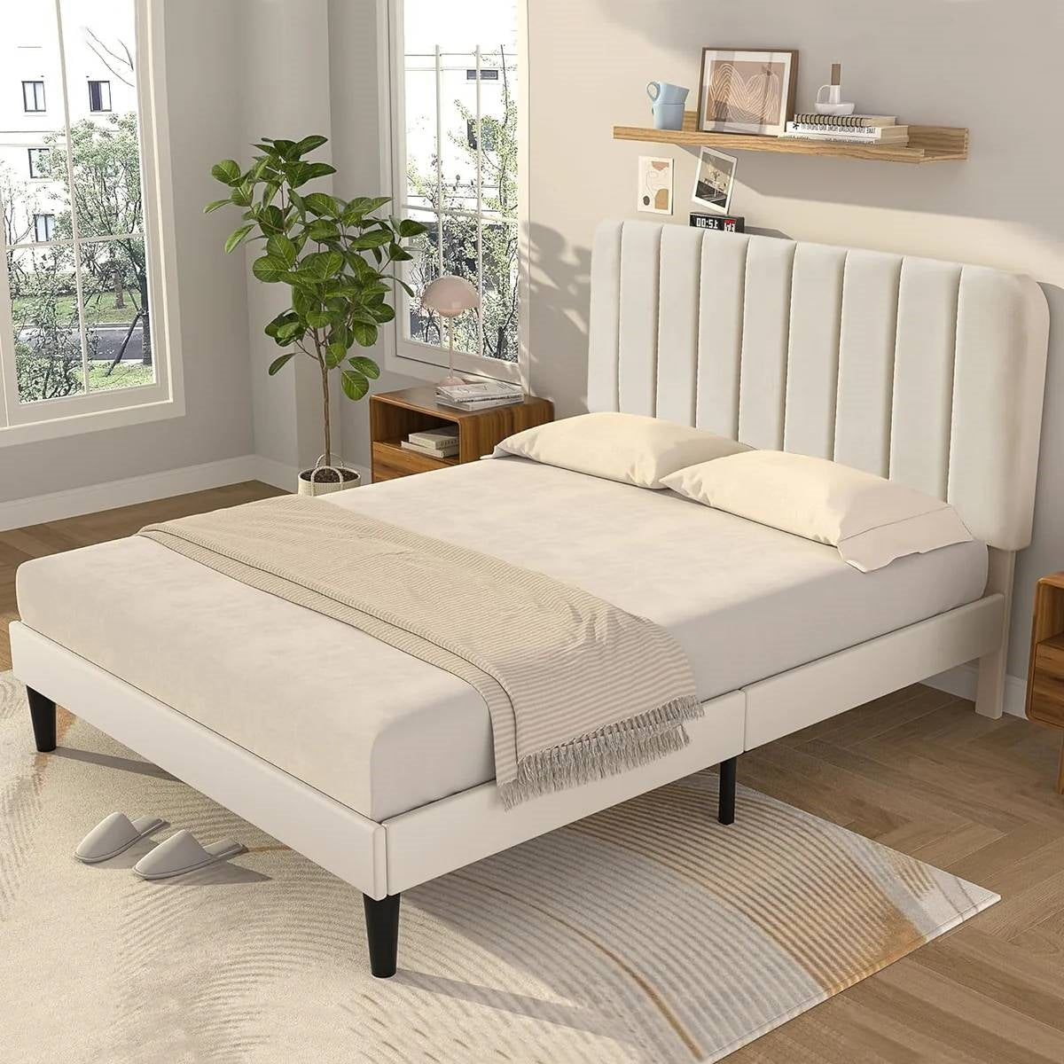 Beige upholstered bed in a bedroom setting with a plant and shelves.