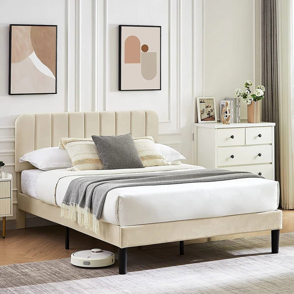 Beige upholstered bed in a bedroom with white walls and decor.