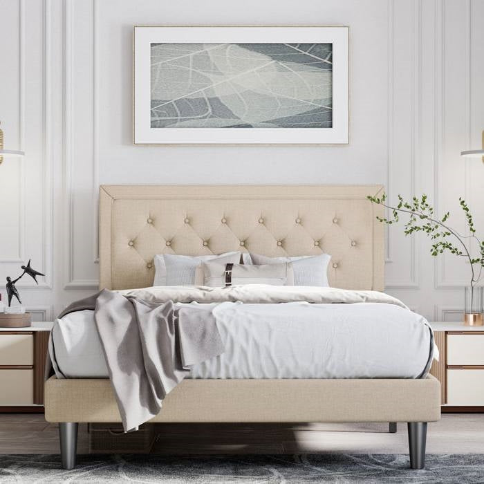 Beige upholstered bed in a bedroom setting with a framed abstract art piece on the wall.
