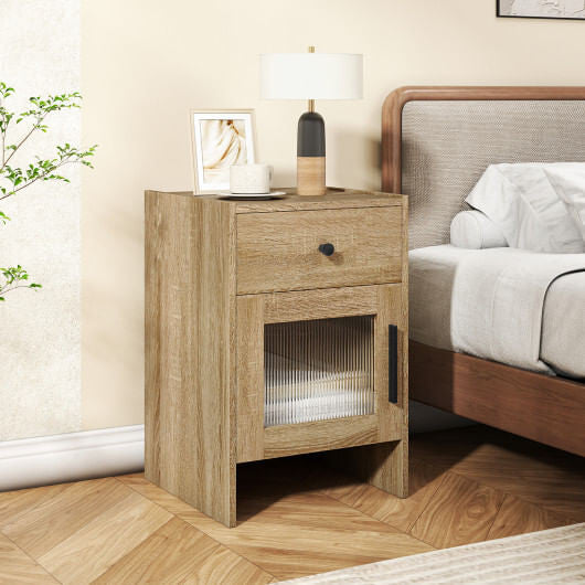 Wooden nightstand with a lamp and framed picture next to a bed in a bedroom setting.