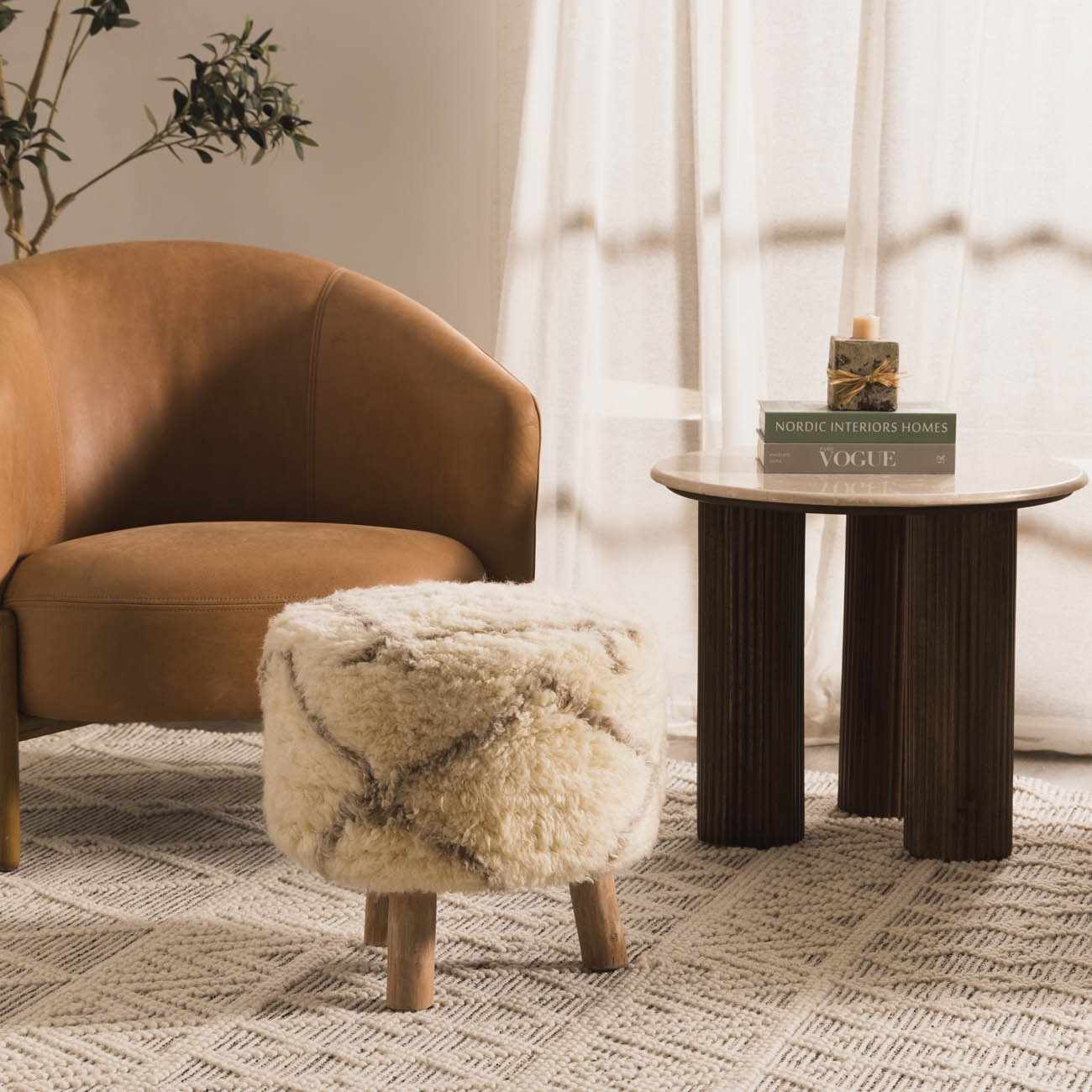 Brown armchair with a fluffy ottoman and a small wooden table in a room with curtains and a plant.
