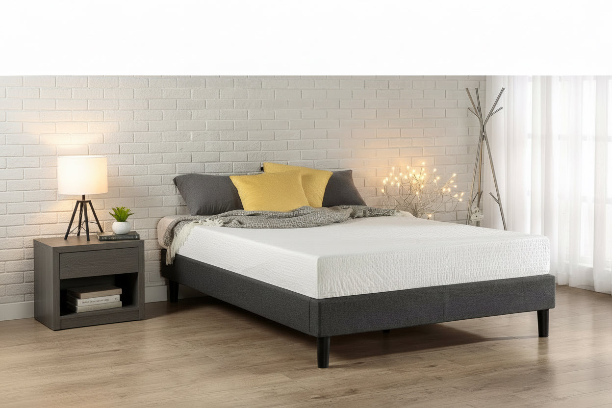 Bed with gray frame and white mattress in a room with a brick wall and wooden floor.
