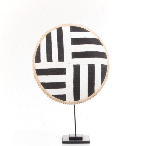 Round woven mat with black and white stripes on a stand against a white background