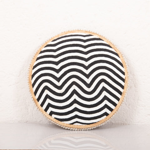 Round woven mat with black and white wavy pattern on a light background