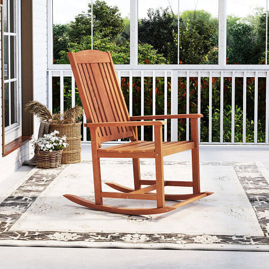 Wooden rocking chair on a porch with a white railing and greenery in the background.