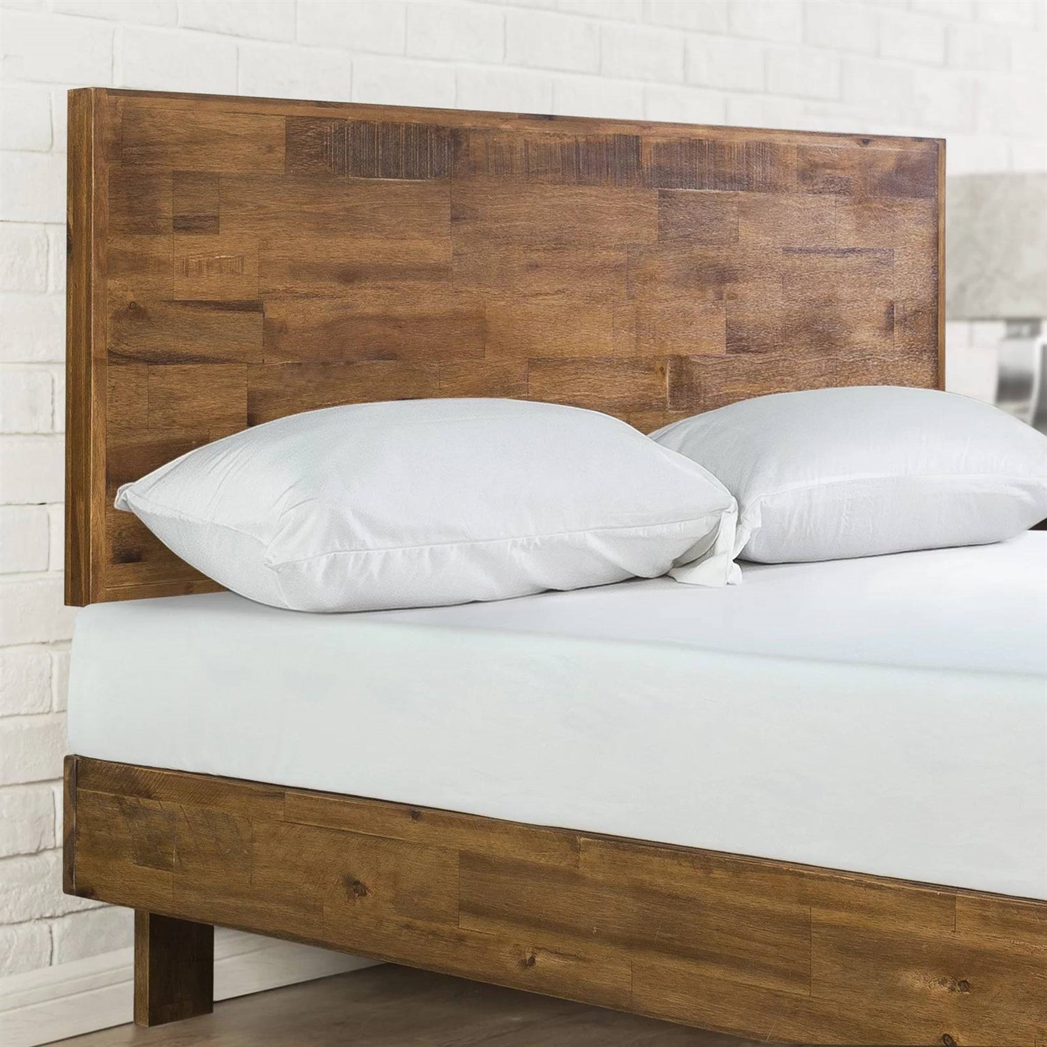 Wooden bed with white bedding against a white brick wall