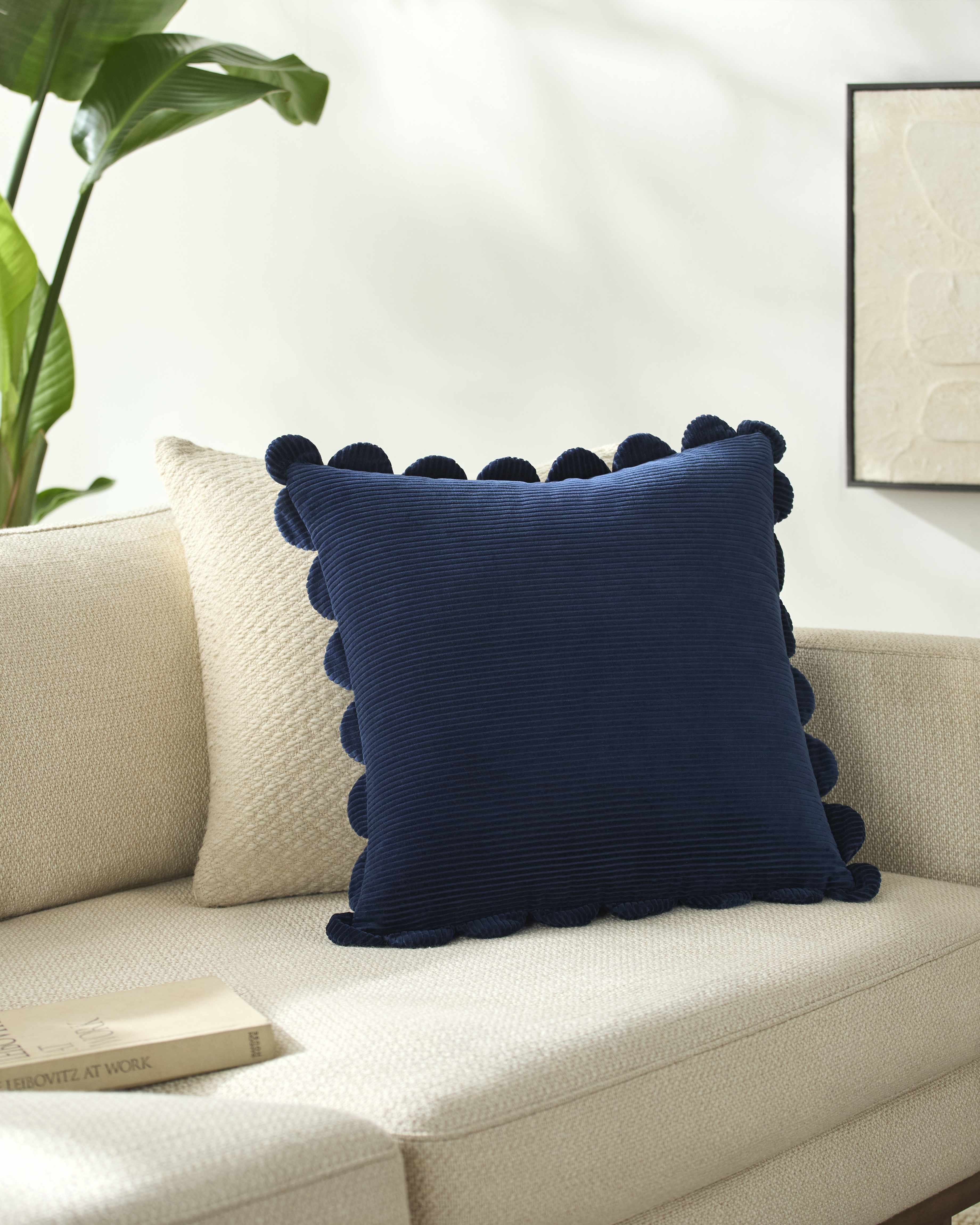 Navy blue pillow with pom-pom details on a beige sofa