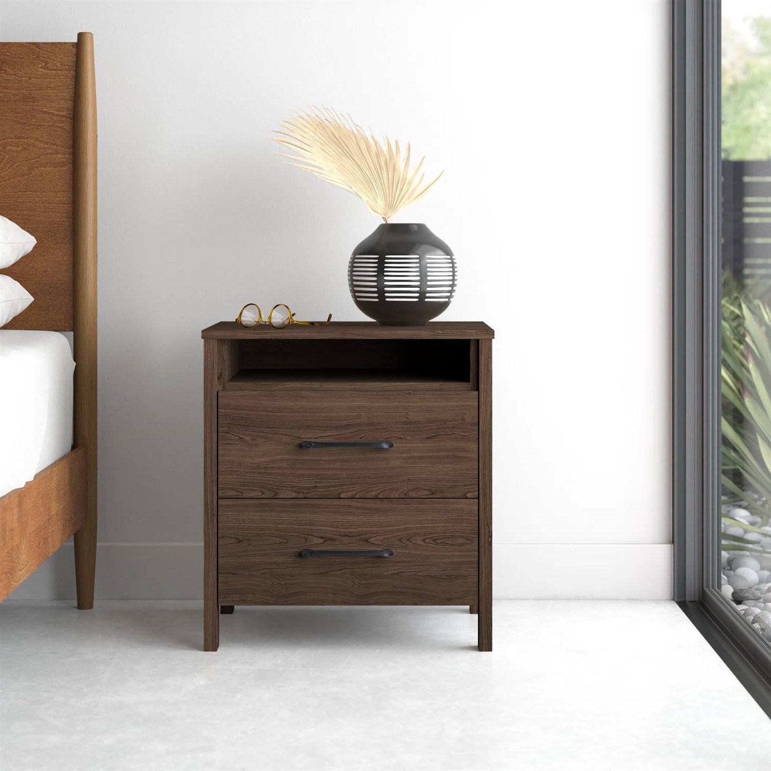 Wooden nightstand with decorative items next to a bed in a bedroom.