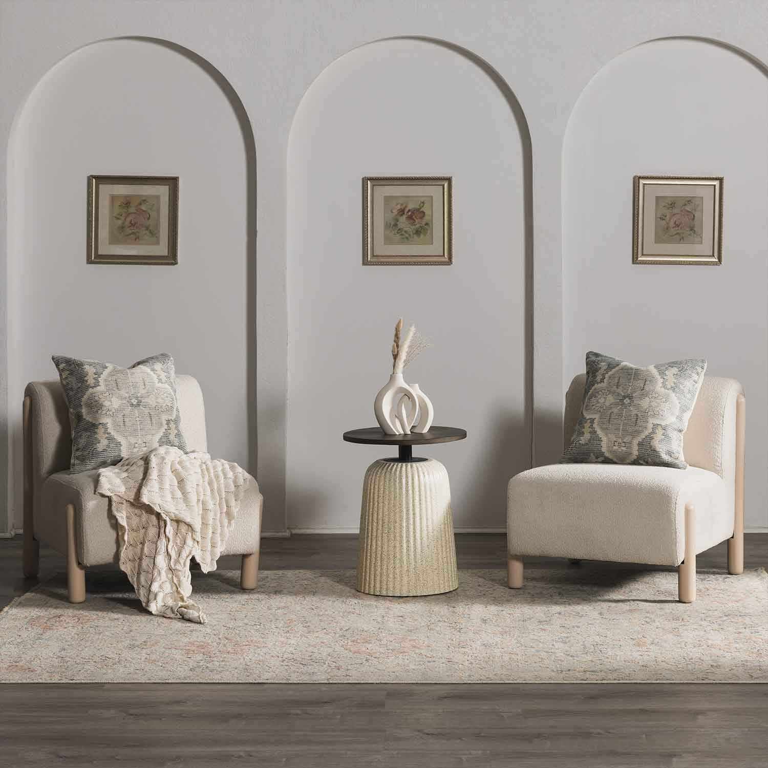Two armchairs with decorative pillows and a small table in a room with arched doorways and framed artwork on the walls.