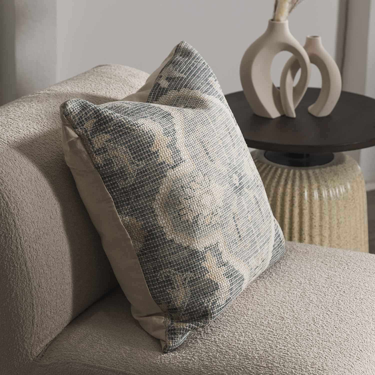 Decorative pillow on a beige sofa with a side table and vases in the background