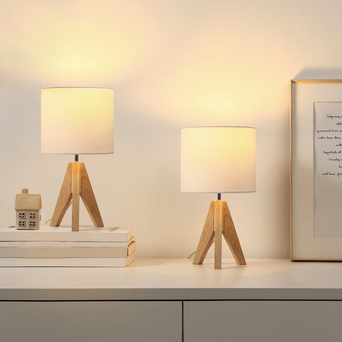 Two small table lamps with wooden bases on a surface, one on books and one on a flat surface.