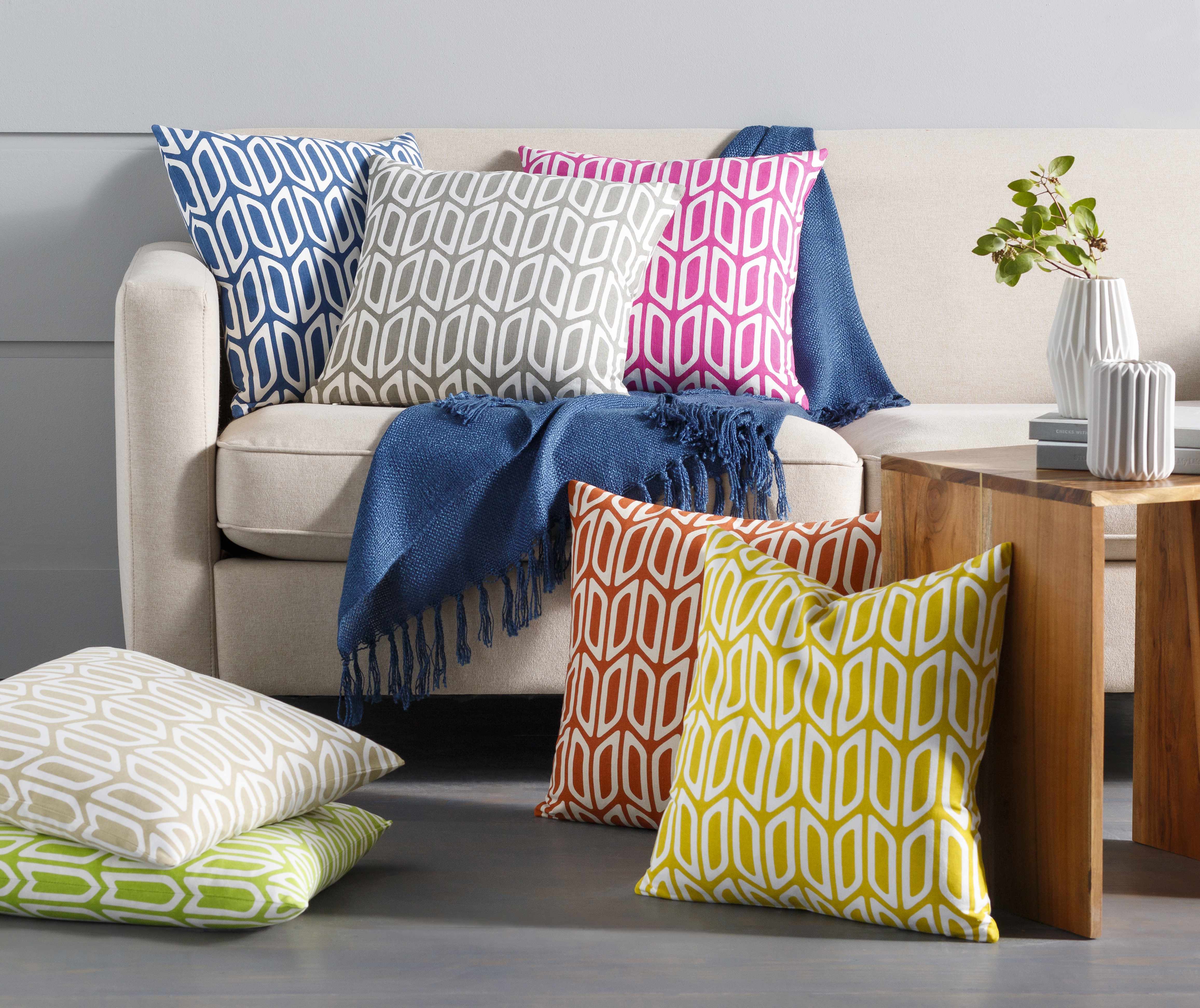 Colorful geometric-patterned pillows on a beige sofa with a wooden side table.