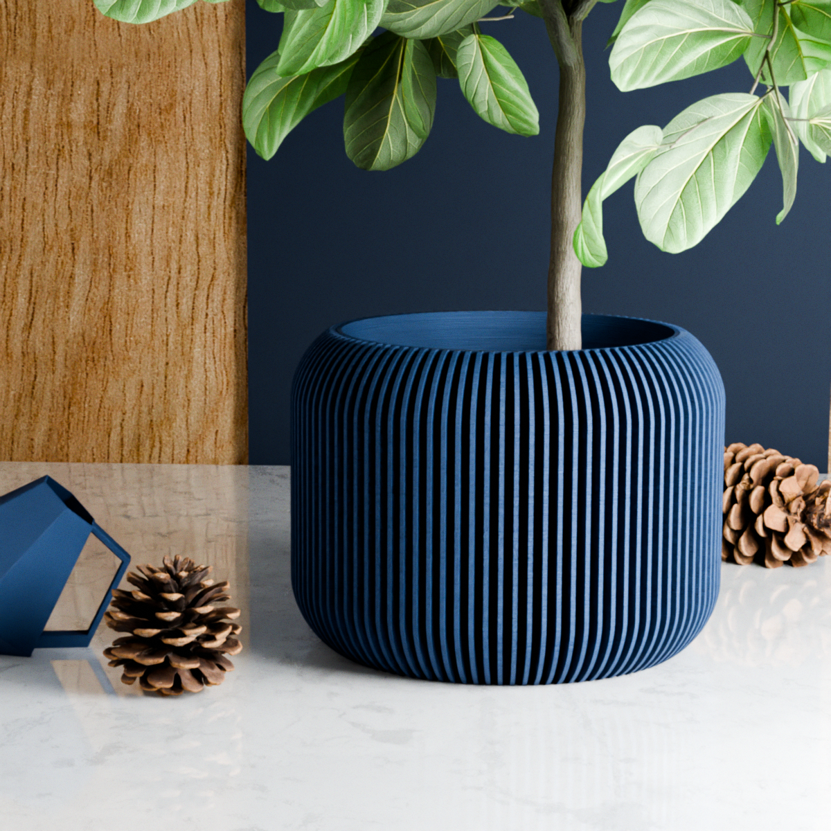 Blue ribbed planter with a plant on a white surface with pinecones and a wooden block.
