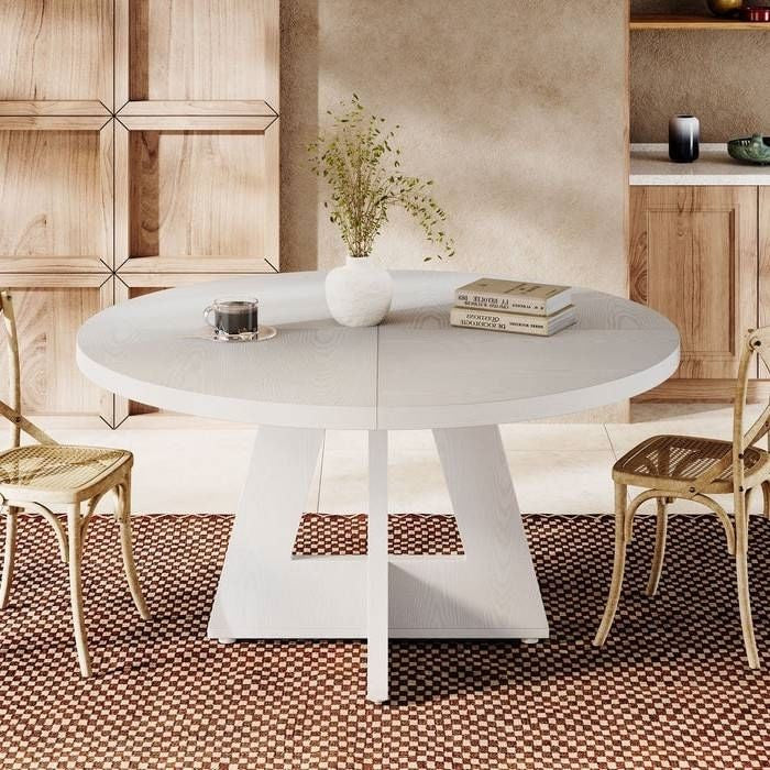Round white dining table with books and a vase in a modern kitchen setting.