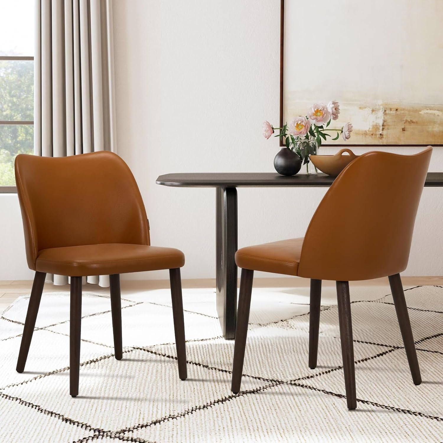 Two brown chairs around a round dining table with a vase of flowers in a room.