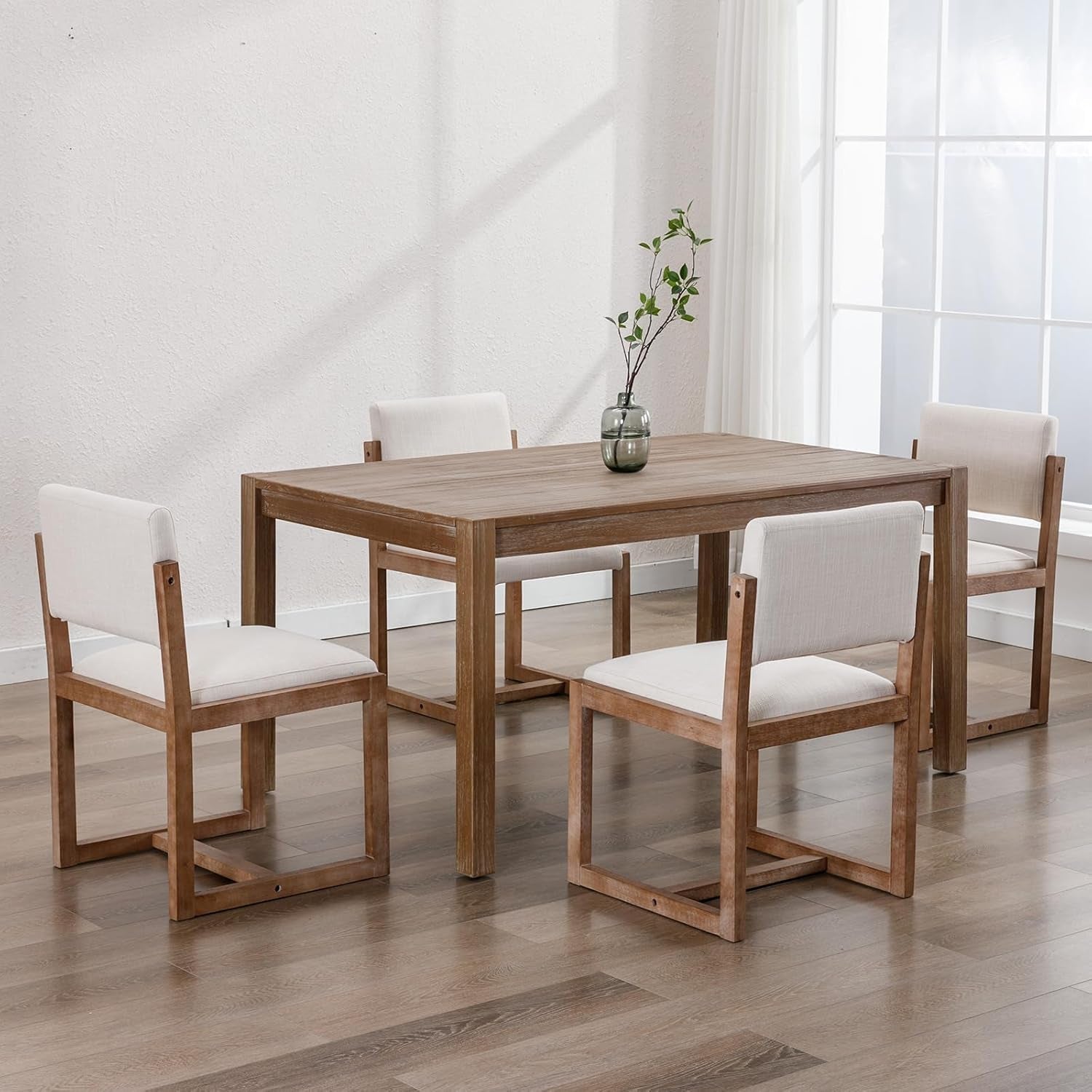 Dining table set with wooden chairs and white cushions in a bright room.