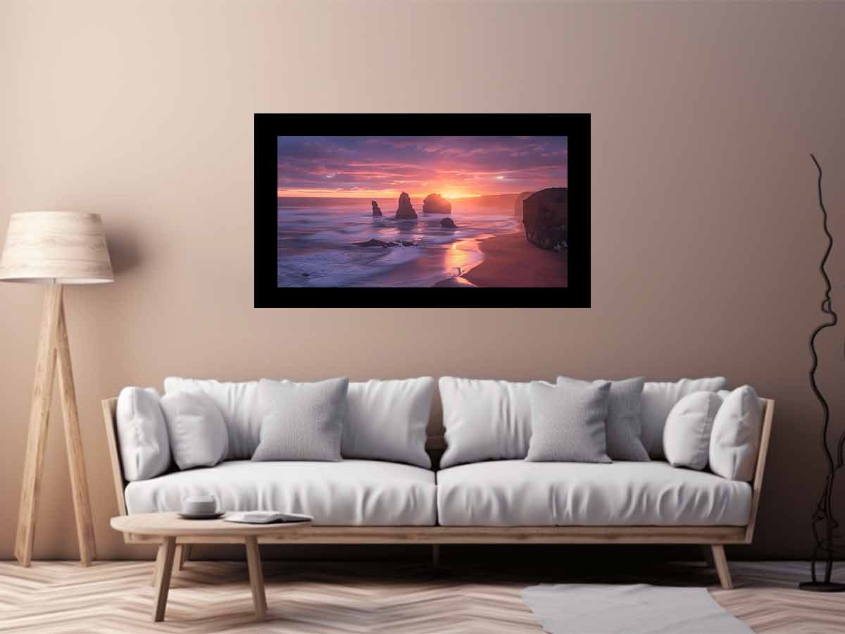 Framed artwork of a sunset over a beach with rocks on a wall above a white sofa.