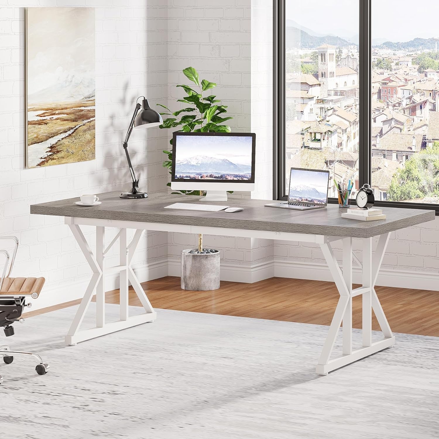 Modern office desk with computer setup in a bright room with large windows.