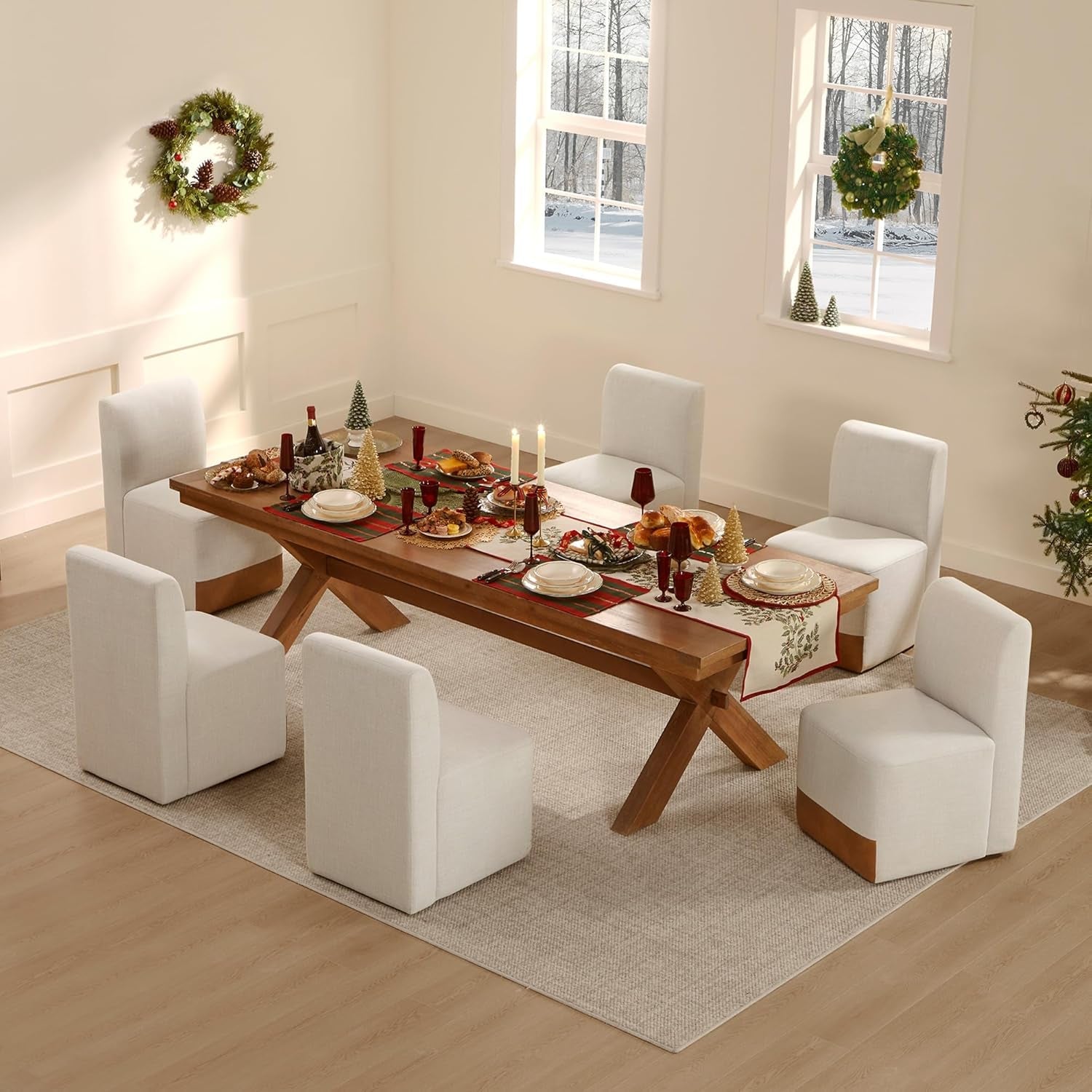 Dining room with a wooden table set for a meal, surrounded by white chairs, with Christmas decorations.