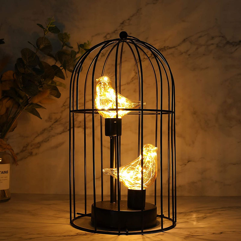 Decorative lamp with glowing bulbs inside a black cage on a marble surface.