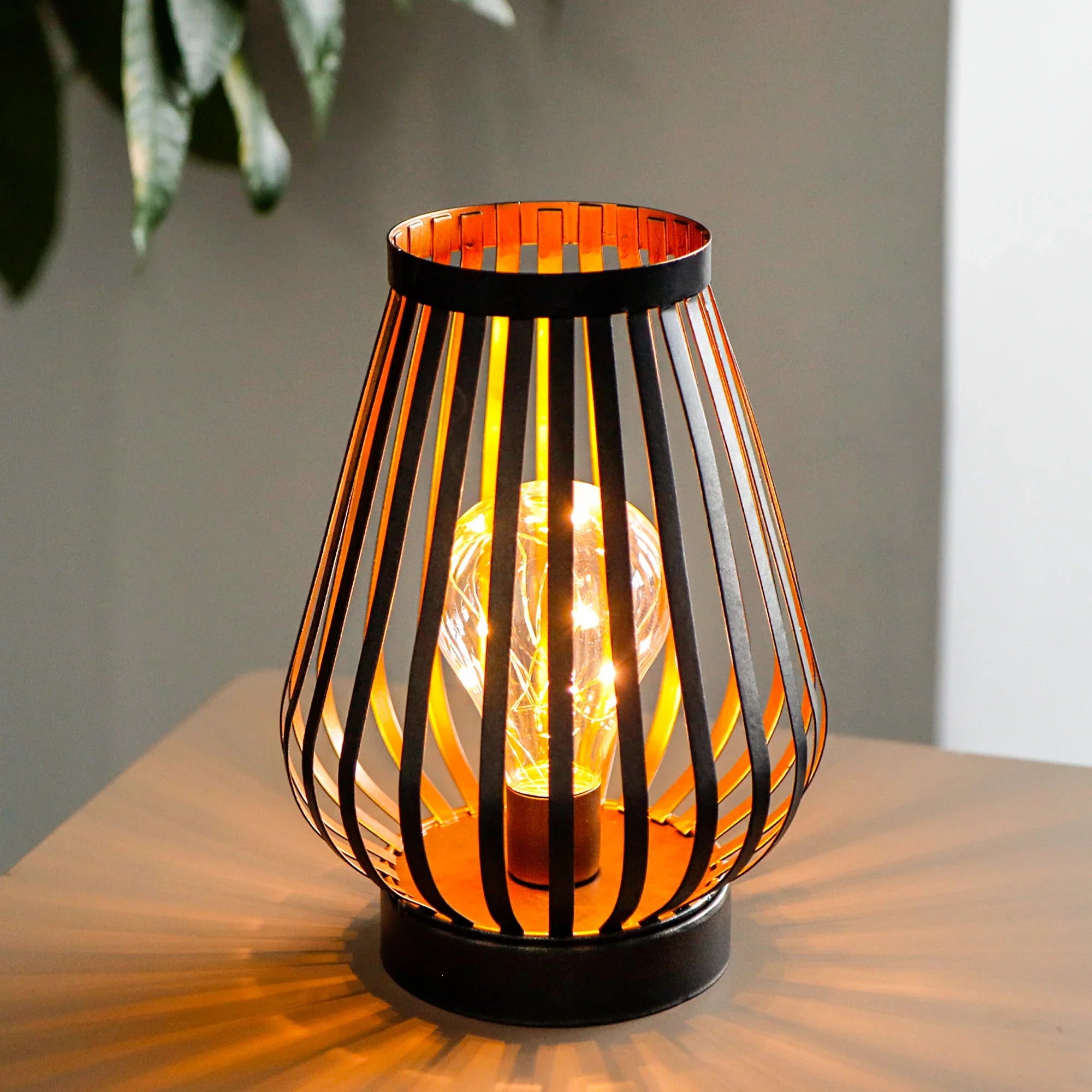 Decorative lamp with a wire cage design on a wooden surface.